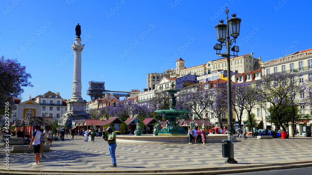 Rossio Platz in Lissabon mit  hoher Säule mit Pedro IV. in Portugal und blau blühenden Jacarandabäumen
