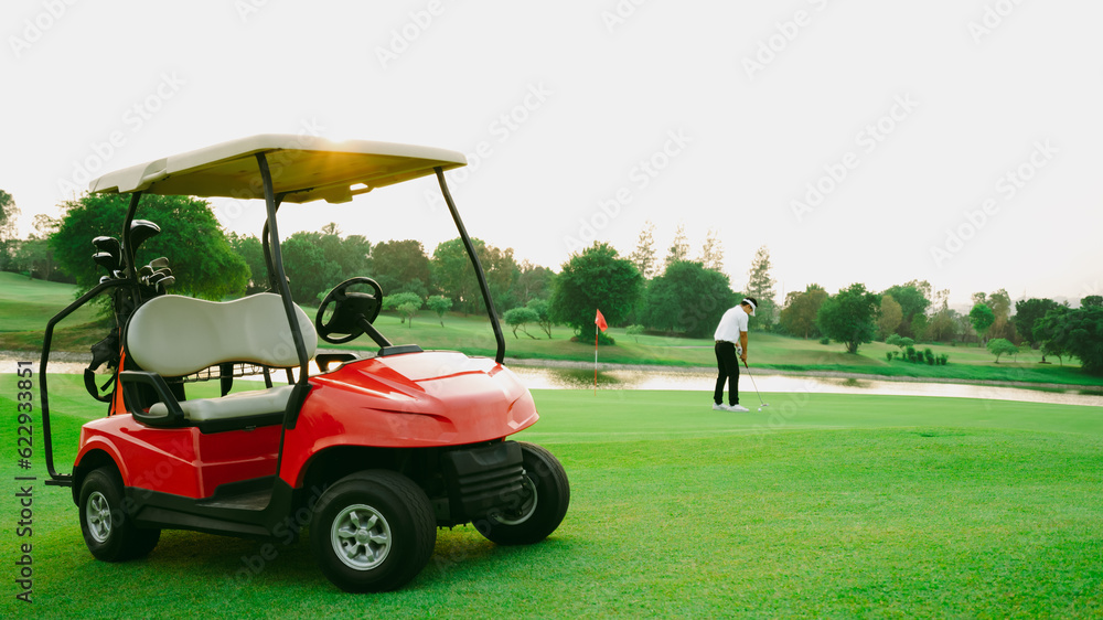 Red golf cart on golf course with green grass and golfer is putter golf in background.
