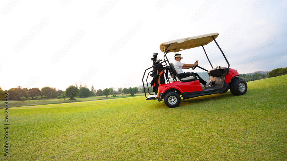 Fototapeta premium Side view of golfers riding golf cart on golf course with green grass at warm sunny day.