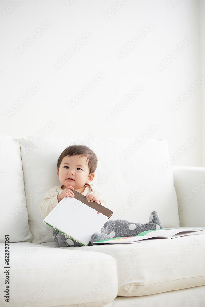 白いソファの上で絵本を持つ赤ちゃん 白いソファの上で絵本を持つ赤ちゃん