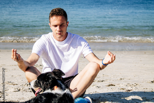 young man with his dog on the beach doing meditation or yoga © tetxu