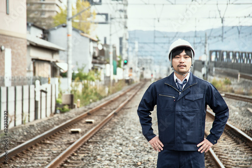 線路をバックに立つ作業服とヘルメットの男性 photo