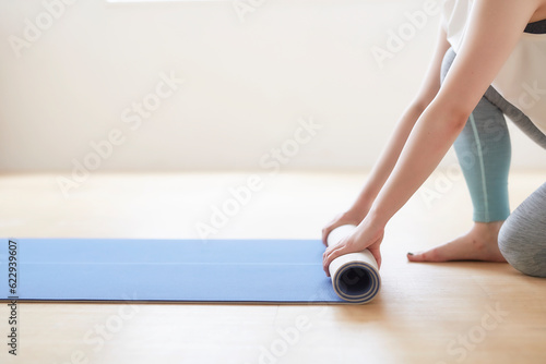 床でヨガマットを丸めている女性の手元