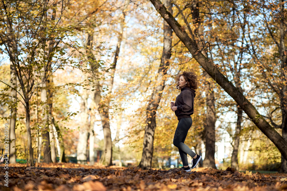 Wide shot of caucasian woman jogging in the park in the autumn Wide shot of caucasian woman jogging in the park in the autumn