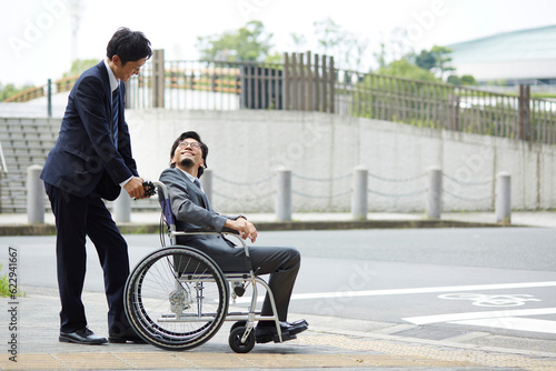 車椅子の男性を押しているスーツの男性 photo