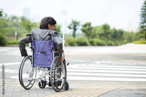 車椅子に乗るスーツ姿の男性と道路 photo