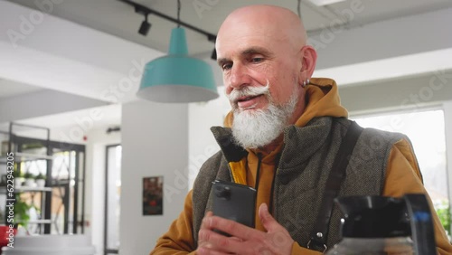 A modern old man with a beard and mustache pays with a smartphone in a coffee shop or cafe. Senior buys coffee or tea take evey. Morning coffee outside for breakfast. NFC wireless technologies photo