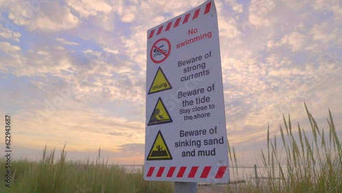 Slow approach to warning sign at seaside at sunset. Beware strong currents, tides, sinking sand and mud. Fleetwood, Wyre, Lancashire, England, UK. Sony FX30 photo