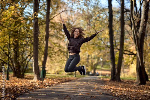 Wide shot of caucasian woman jumping in the park in the autumn   with arms outstretched