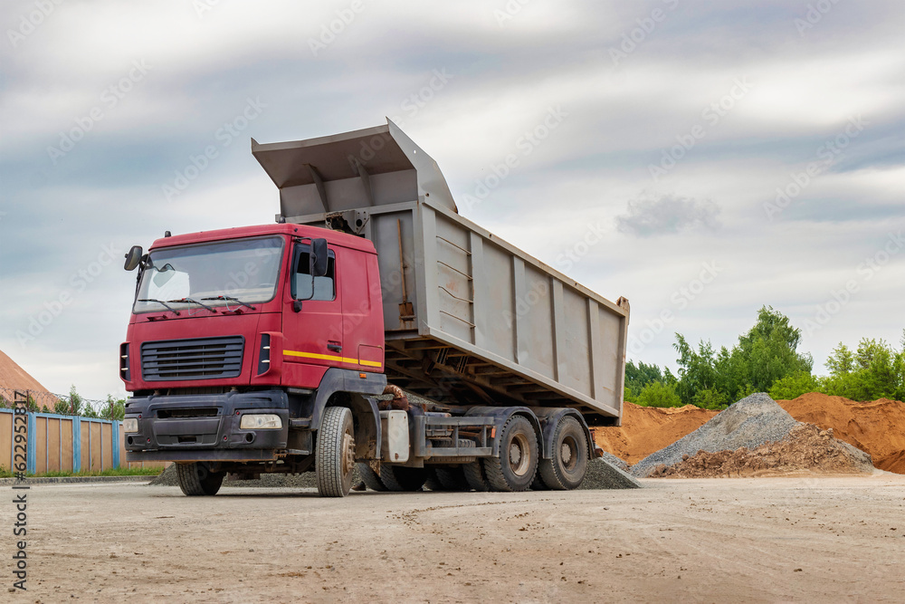 Dump truck with a raised body at a construction site. Transportation and unloading of sand or soil. Technique for transportation of bulk materials. Transportation of bulk building materials. Dump truck with a raised body at a construction site. Transportation and unloading of sand or soil. Technique for transportation of bulk materials. Transportation of bulk building materials.