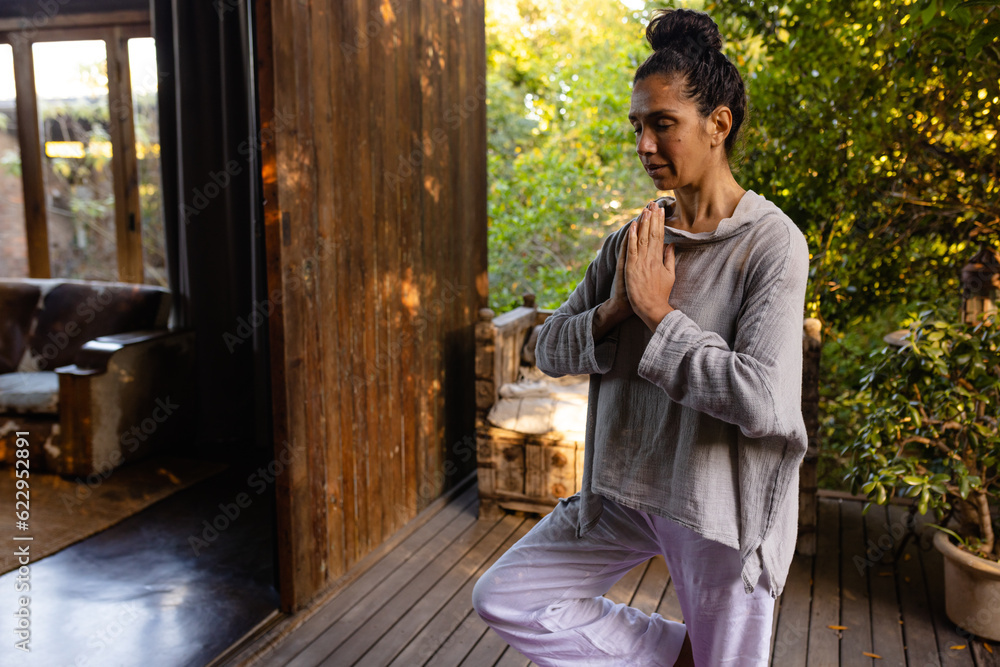 Biracial woman doing yoga, meditating on terrace in garden Biracial woman doing yoga, meditating on terrace in garden