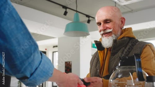 A modern old man with a beard and mustache pays with a smartphone in a coffee shop or cafe. Senior buys coffee or tea take evey. Morning coffee outside for breakfast. NFC wireless technologies photo