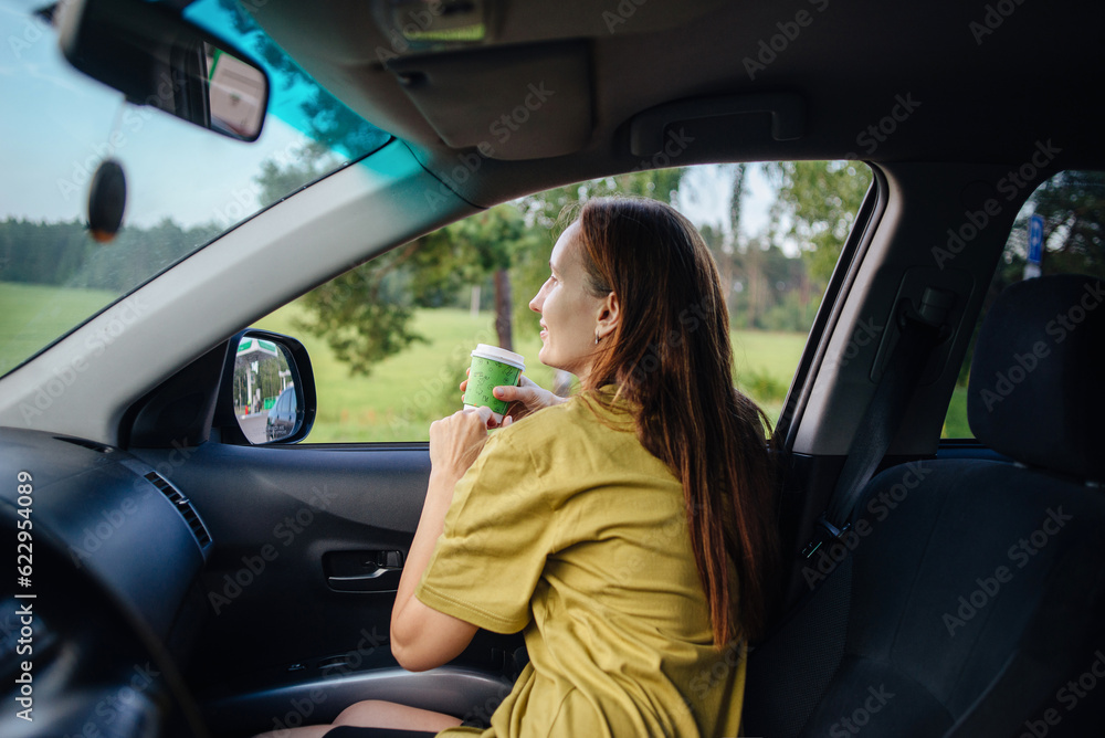 A girl on a trip sits in her car drinking coffee
