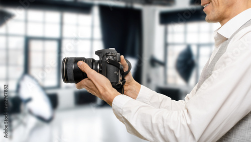 Closeup of smiling male photographer with professional camera working in photo studio, The photographer's hands are a testament to experience and expertise