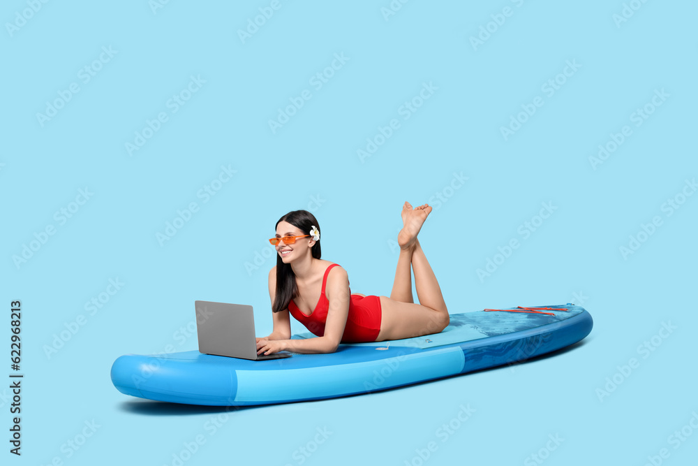 Obraz premium Happy woman with laptop on SUP board against light blue background