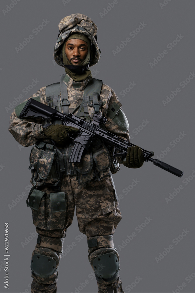 Confident soldier in NATO uniform and helmet poses with his rifle on a plain grey background, showcasing the courage and strength of military personnel Confident soldier in NATO uniform and helmet poses with his rifle on a plain grey background, showcasing the courage and strength of military personnel