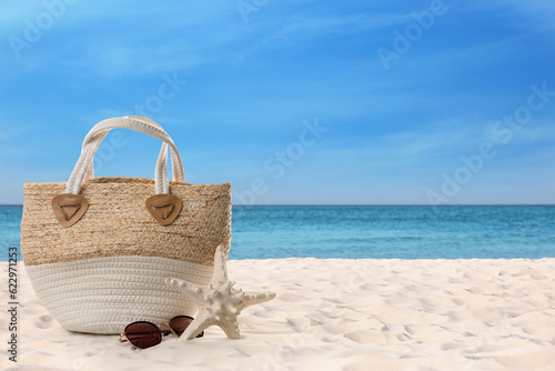 Bag with sunglasses and starfish on sunny ocean beach, space for text. Summer vacation