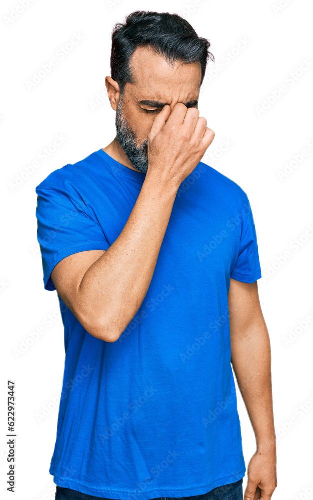 Middle aged man with beard wearing casual blue t shirt tired rubbing nose and eyes feeling fatigue and headache. stress and frustration concept. Middle aged man with beard wearing casual blue t shirt tired rubbing nose and eyes feeling fatigue and headache. stress and frustration concept.