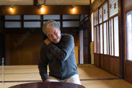 田舎の家で肩を押さえるシニア男性 photo