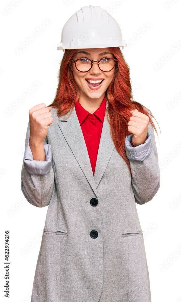 Young redhead woman wearing architect hardhat celebrating surprised and amazed for success with arms raised and open eyes. winner concept. Young redhead woman wearing architect hardhat celebrating surprised and amazed for success with arms raised and open eyes. winner concept.