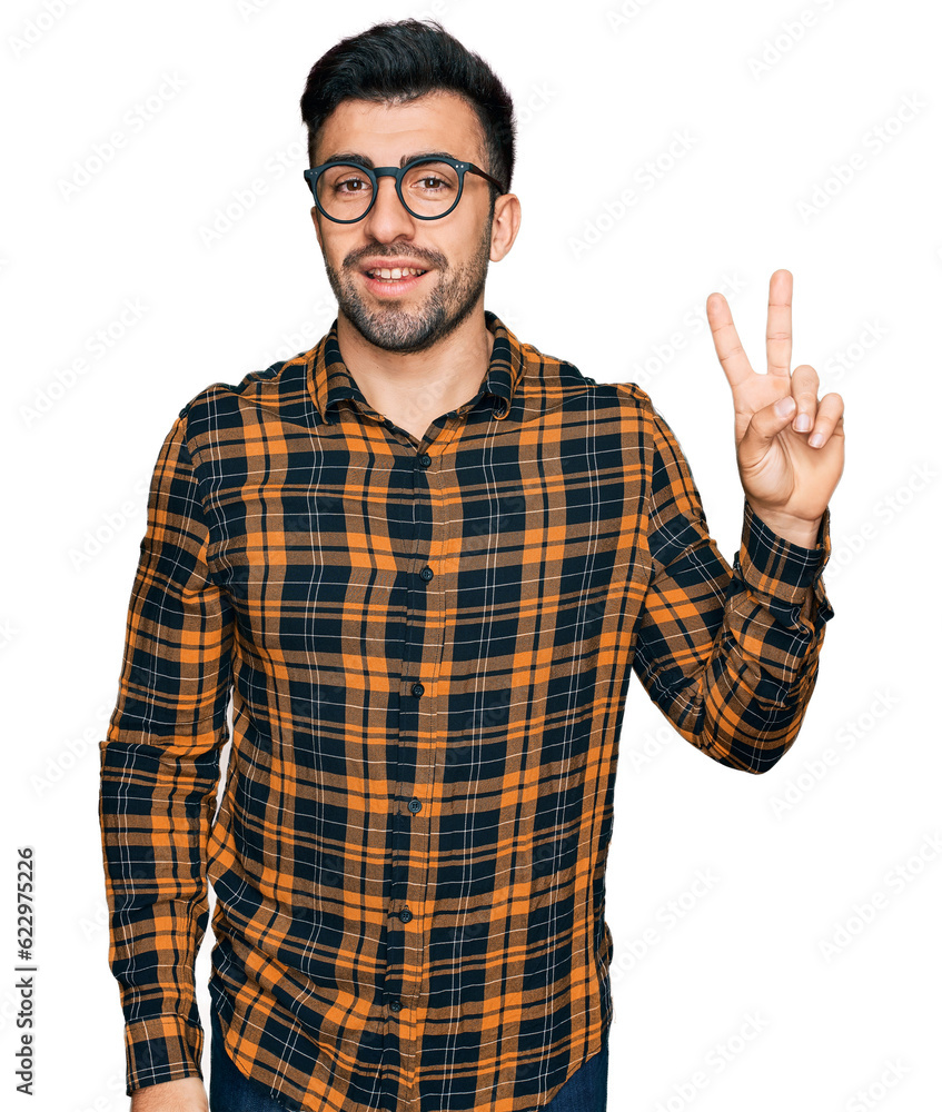 Hispanic man with beard wearing casual clothes and glasses smiling with happy face winking at the camera doing victory sign. number two. Hispanic man with beard wearing casual clothes and glasses smiling with happy face winking at the camera doing victory sign. number two.