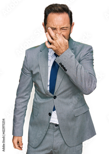 Middle age man wearing business clothes smelling something stinky and disgusting, intolerable smell, holding breath with fingers on nose. bad smell