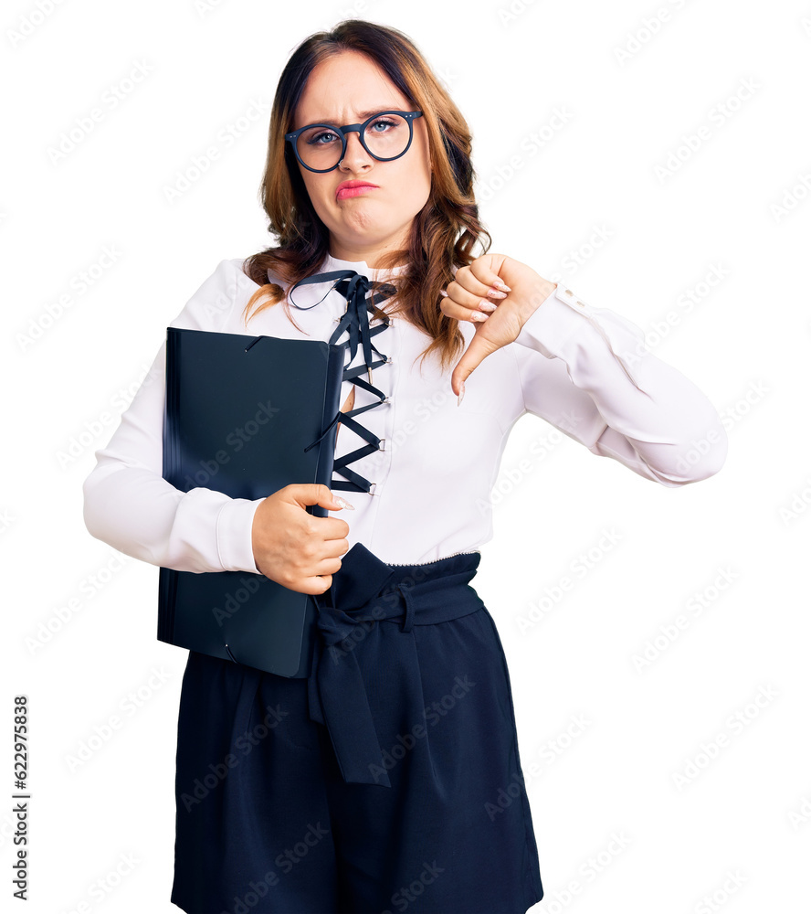 Young beautiful caucasian woman wearing business shirt and glasses holding folder with angry face, negative sign showing dislike with thumbs down, rejection concept Young beautiful caucasian woman wearing business shirt and glasses holding folder with angry face, negative sign showing dislike with thumbs down, rejection concept