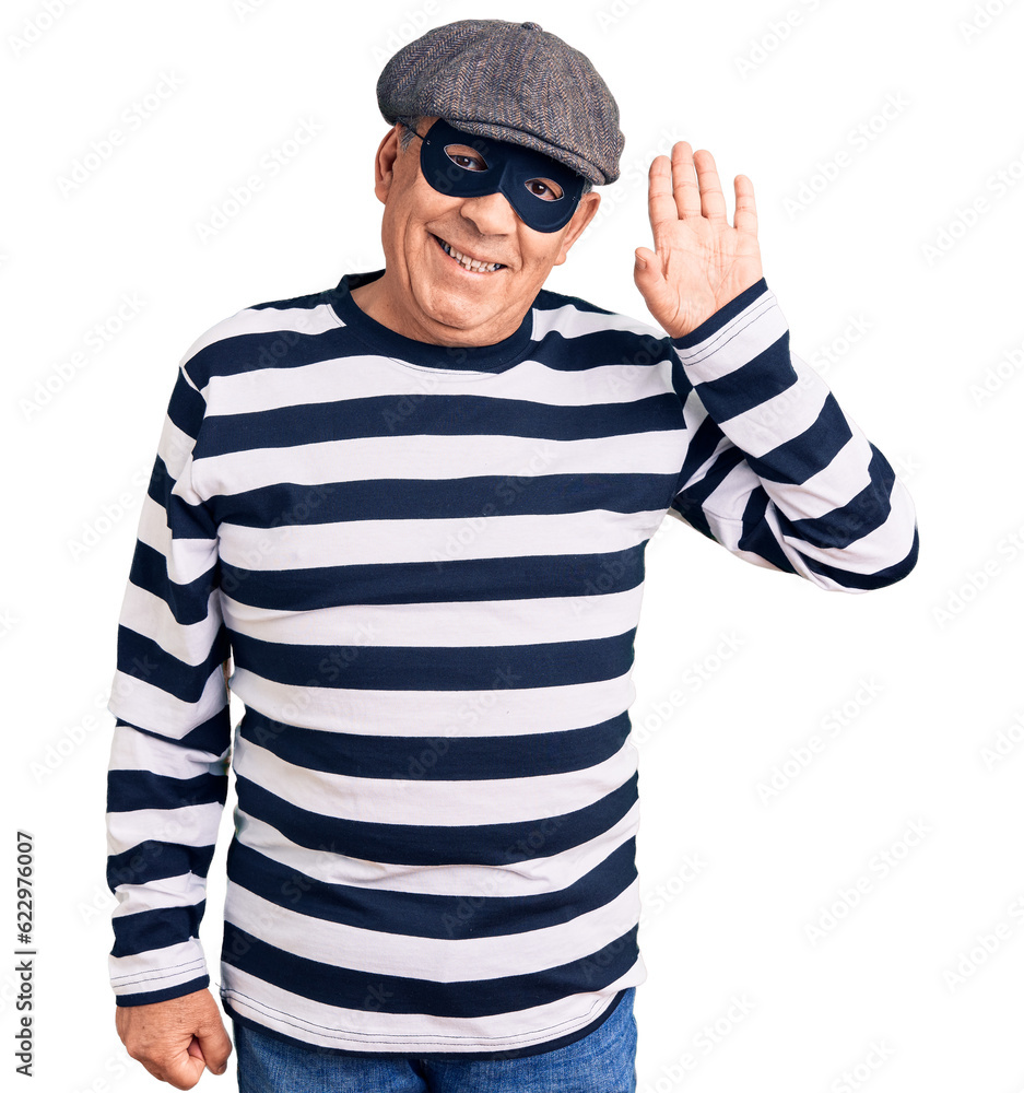 Senior handsome man wearing burglar mask and t-shirt waiving saying hello happy and smiling, friendly welcome gesture Senior handsome man wearing burglar mask and t-shirt waiving saying hello happy and smiling, friendly welcome gesture