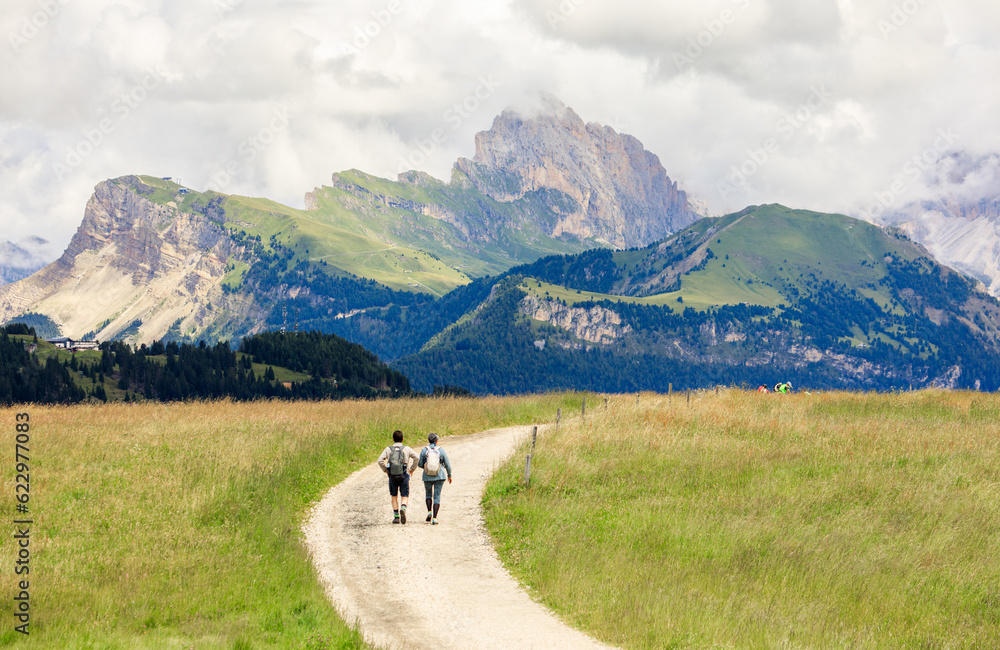 Couple of tourists walking in thevalley of Alpe di Suisi mountains in South Tyrol, Italy.