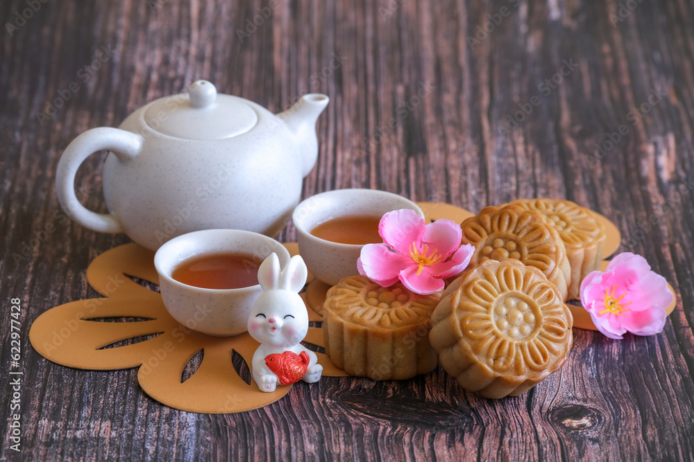 Chinese Mid-Autumn Festival concept made from mooncakes, tea decorated with plum blossom and rabbits on wooden background. Chinese Mid-Autumn Festival concept made from mooncakes, tea decorated with plum blossom and rabbits on wooden background.