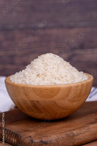 Rice on wood background. Uncooked dry rice in wooden bowl. Close up