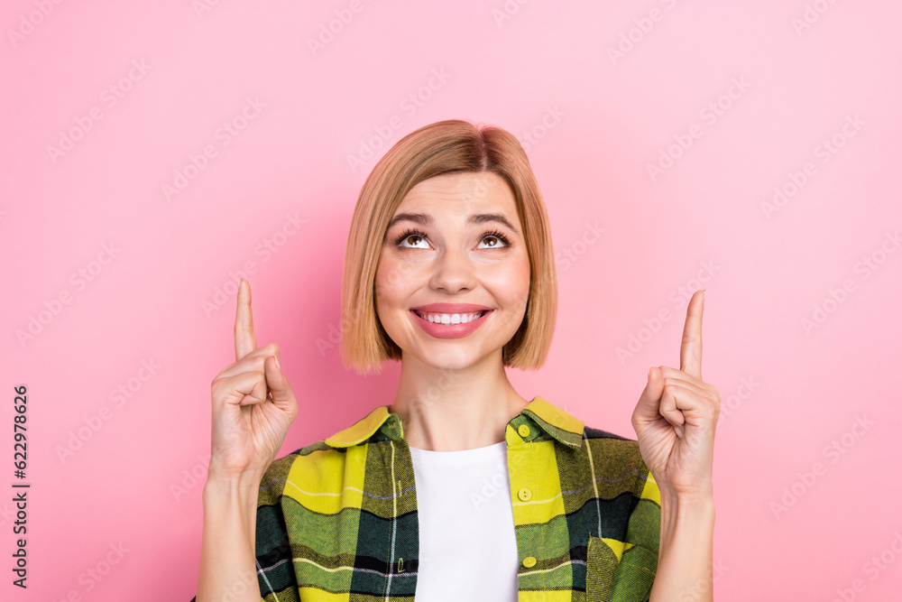 Photo of cheerful nice girl beaming smile indicate fingers up empty space isolated on pink color background Photo of cheerful nice girl beaming smile indicate fingers up empty space isolated on pink color background