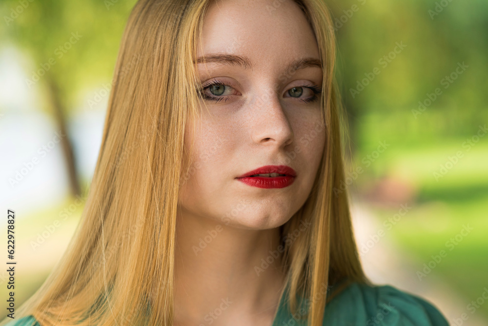 Naklejka premium Portrait of a girl in a green dress on a walk on a sunny summer day in the park.