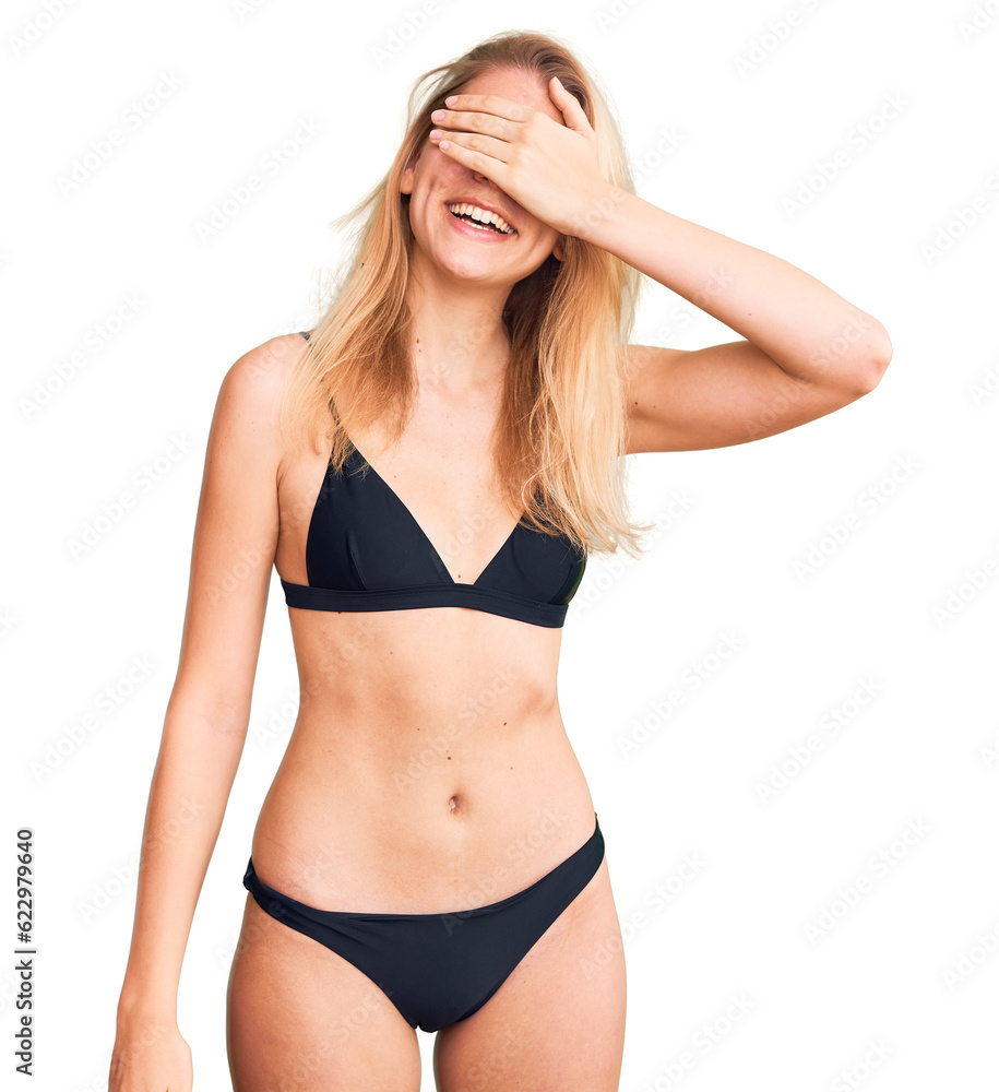 Young beautiful blonde woman wearing bikini smiling and laughing with hand on face covering eyes for surprise. blind concept. Young beautiful blonde woman wearing bikini smiling and laughing with hand on face covering eyes for surprise. blind concept.