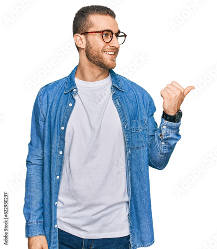 Young caucasian man wearing casual clothes smiling with happy face looking and pointing to the side with thumb up.