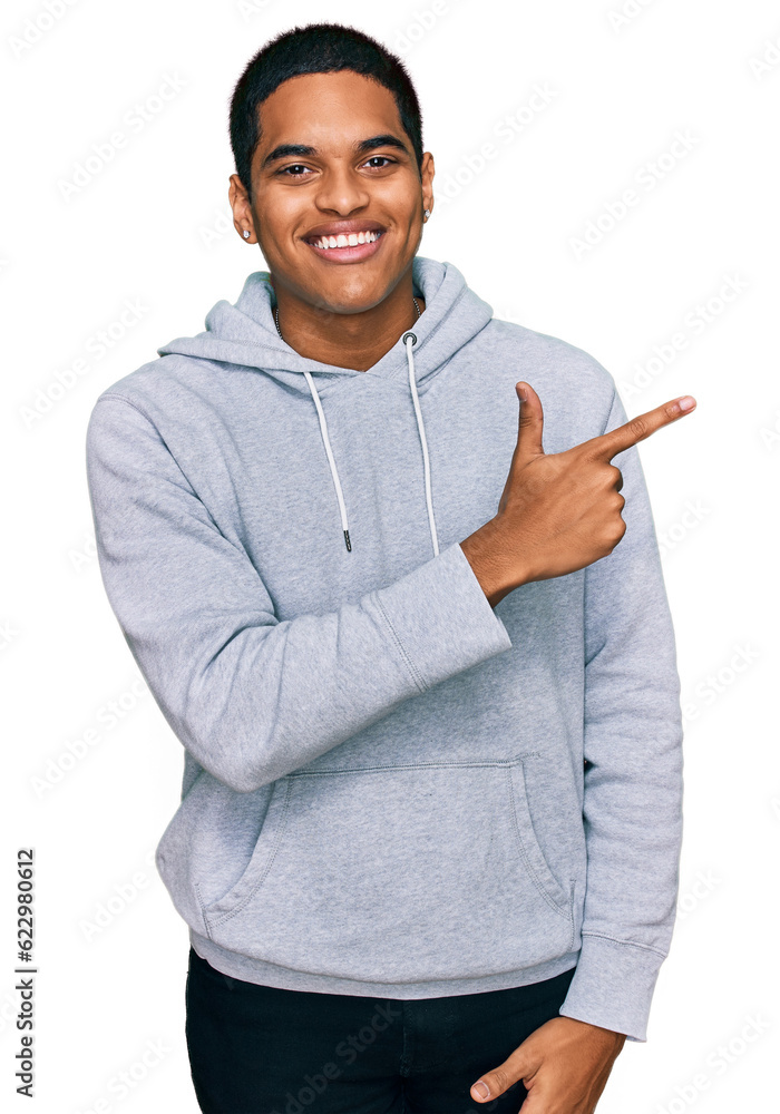 Young handsome hispanic man wearing casual sweatshirt cheerful with a smile of face pointing with hand and finger up to the side with happy and natural expression on face Young handsome hispanic man wearing casual sweatshirt cheerful with a smile of face pointing with hand and finger up to the side with happy and natural expression on face