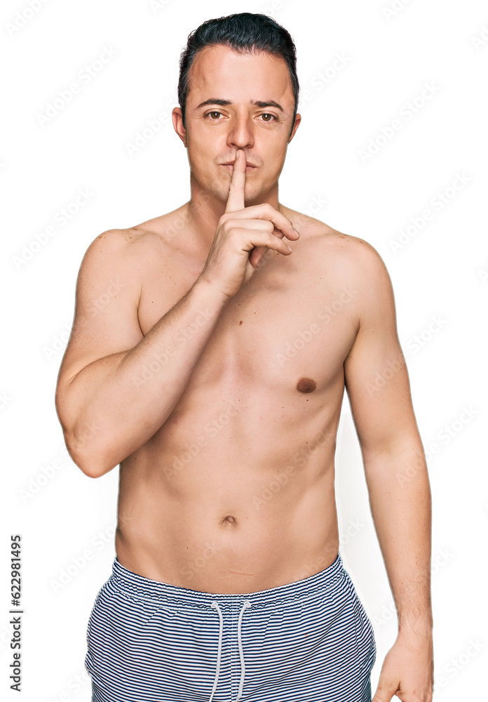 Handsome young man wearing swimwear shirtless asking to be quiet with finger on lips. silence and secret concept. Handsome young man wearing swimwear shirtless asking to be quiet with finger on lips. silence and secret concept.