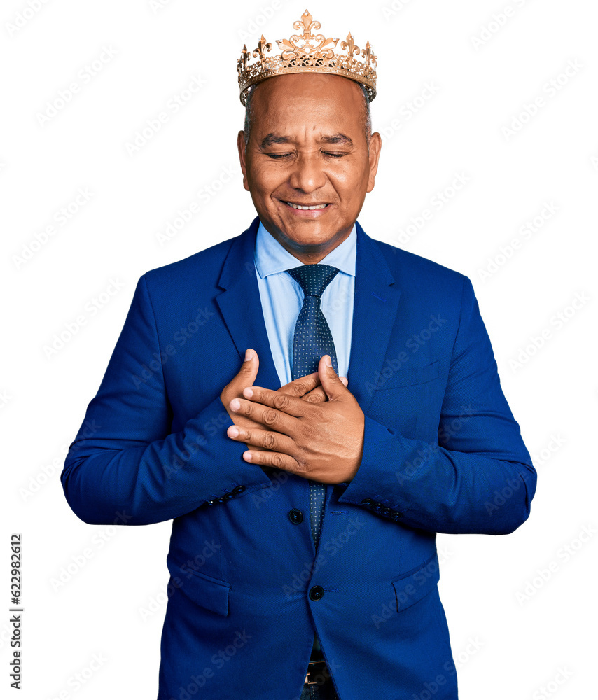 Hispanic middle age man wearing king crown smiling with hands on chest with closed eyes and grateful gesture on face. health concept. Hispanic middle age man wearing king crown smiling with hands on chest with closed eyes and grateful gesture on face. health concept.