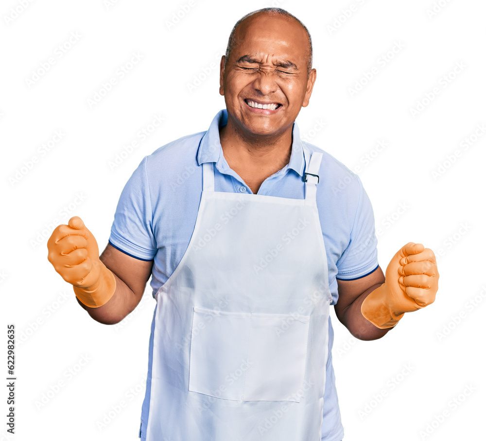 Hispanic middle age man wearing cleaner apron and gloves very happy and excited doing winner gesture with arms raised, smiling and screaming for success. celebration concept. Hispanic middle age man wearing cleaner apron and gloves very happy and excited doing winner gesture with arms raised, smiling and screaming for success. celebration concept.