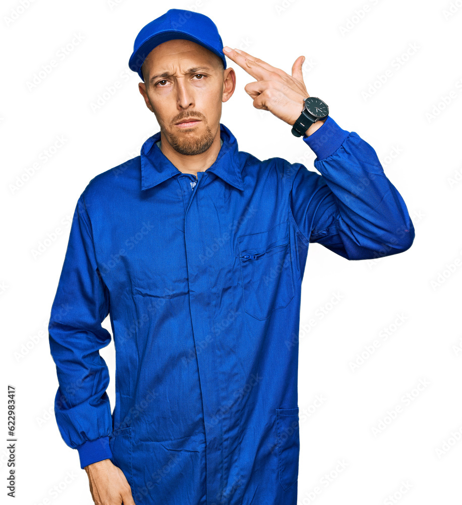Bald man with beard wearing builder jumpsuit uniform shooting and killing oneself pointing hand and fingers to head like gun, suicide gesture.