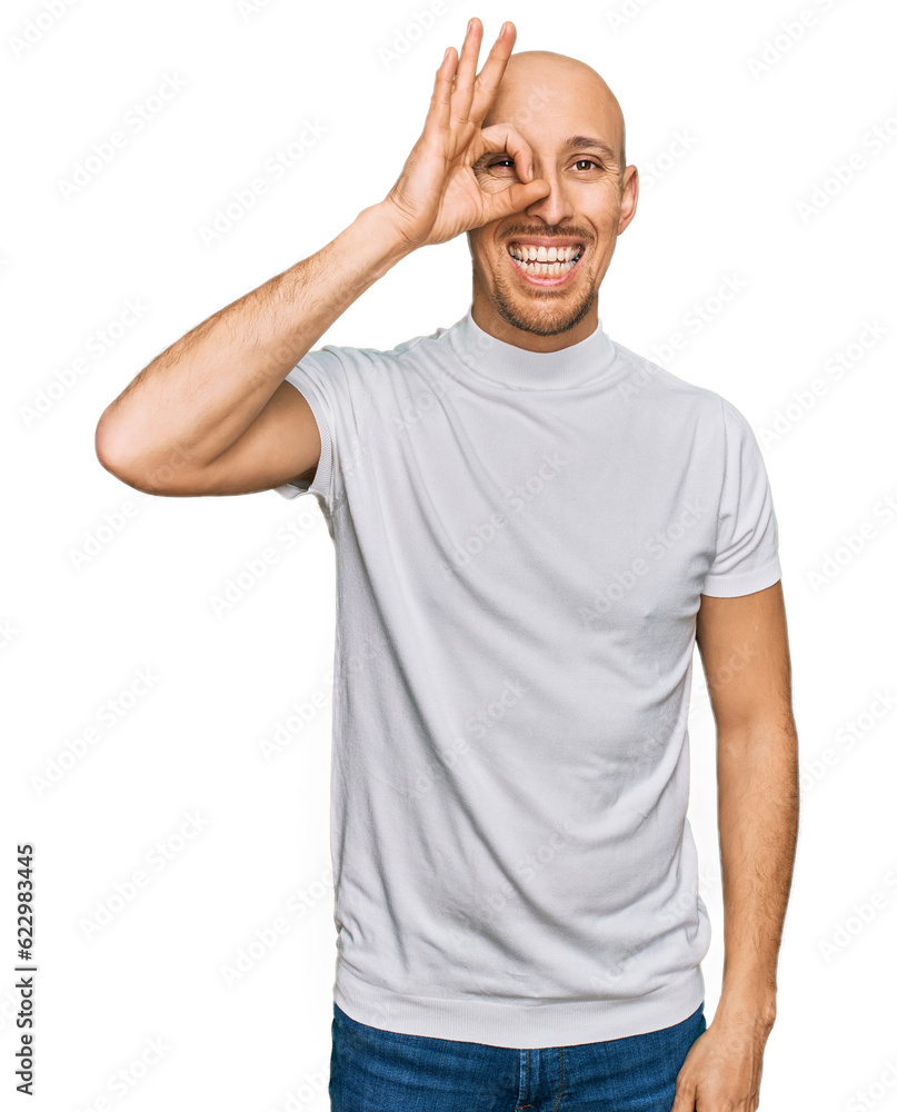Bald man with beard wearing casual white t shirt doing ok gesture with hand smiling, eye looking through fingers with happy face. Bald man with beard wearing casual white t shirt doing ok gesture with hand smiling, eye looking through fingers with happy face.