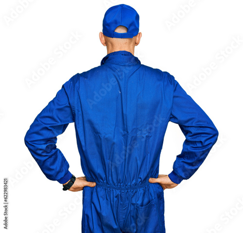 Bald man with beard wearing builder jumpsuit uniform standing backwards looking away with arms on body