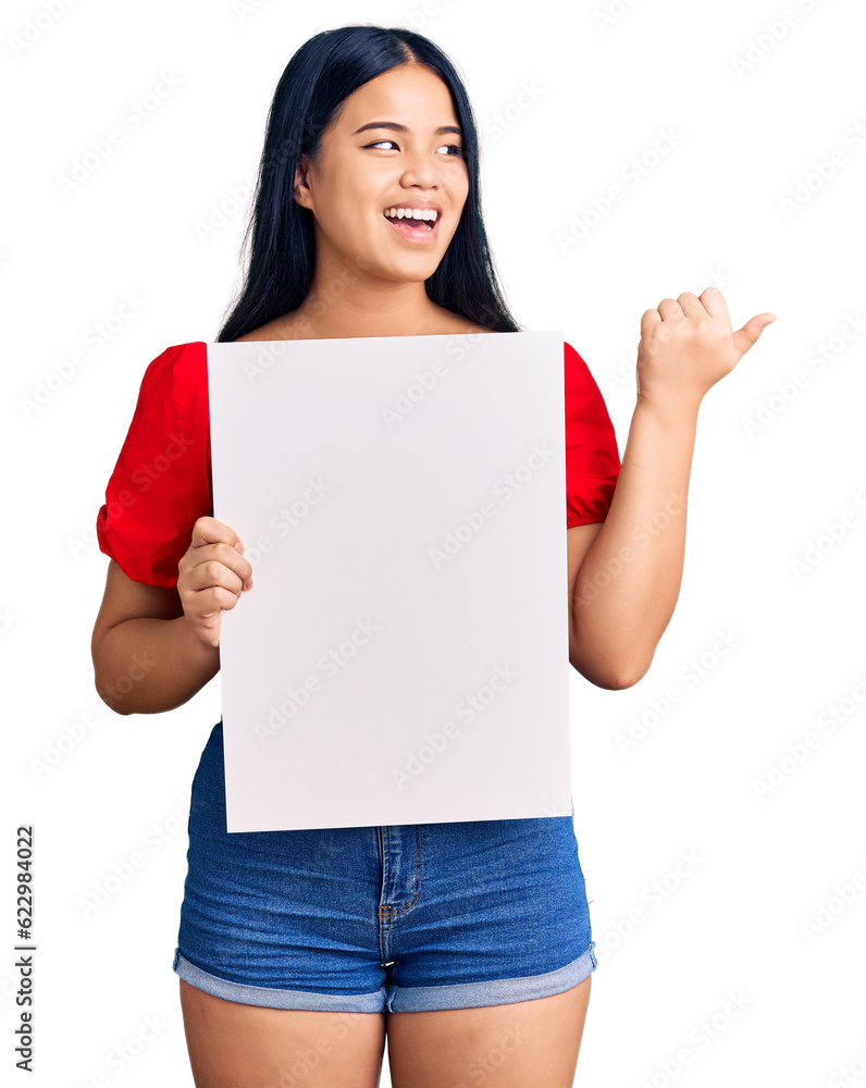 Young beautiful asian girl holding blank empty banner pointing thumb up to the side smiling happy with open mouth Young beautiful asian girl holding blank empty banner pointing thumb up to the side smiling happy with open mouth