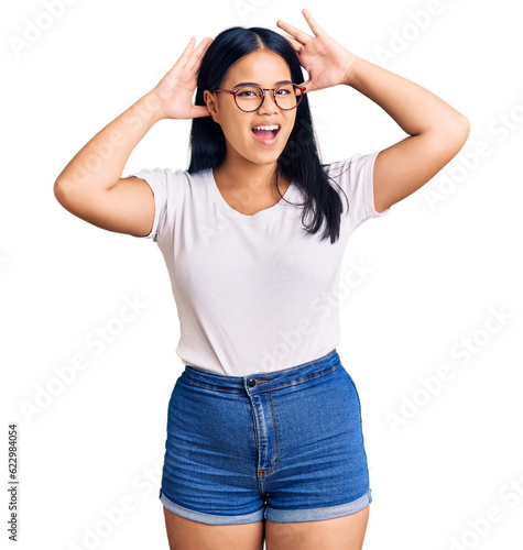 Young beautiful asian girl wearing casual clothes and glasses smiling cheerful playing peek a boo with hands showing face. surprised and exited