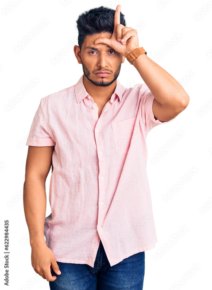 Fototapeta premium Handsome latin american young man wearing casual summer shirt making fun of people with fingers on forehead doing loser gesture mocking and insulting.