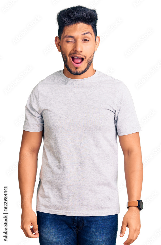 Handsome latin american young man wearing casual tshirt winking looking at the camera with sexy expression, cheerful and happy face. Handsome latin american young man wearing casual tshirt winking looking at the camera with sexy expression, cheerful and happy face.