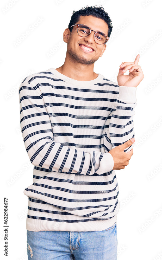 Hispanic handsome young man wearing casual clothes and glasses with a big smile on face, pointing with hand and finger to the side looking at the camera. Hispanic handsome young man wearing casual clothes and glasses with a big smile on face, pointing with hand and finger to the side looking at the camera.