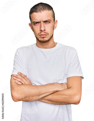 Hispanic young man wearing casual white t shirt skeptic and nervous, disapproving expression on face with crossed arms. negative person.