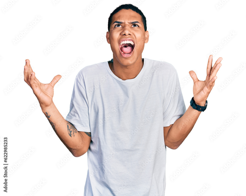 Young hispanic man wearing casual white t shirt crazy and mad shouting and yelling with aggressive expression and arms raised. frustration concept. Young hispanic man wearing casual white t shirt crazy and mad shouting and yelling with aggressive expression and arms raised. frustration concept.
