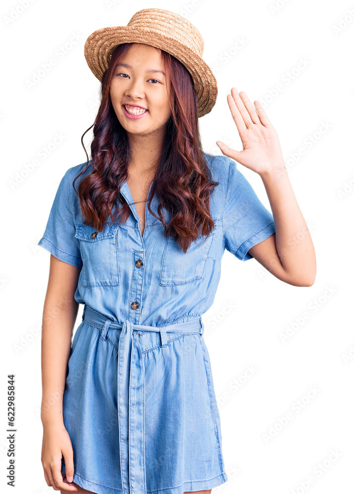 Young beautiful chinese girl wearing summer hat waiving saying hello happy and smiling, friendly welcome gesture Young beautiful chinese girl wearing summer hat waiving saying hello happy and smiling, friendly welcome gesture